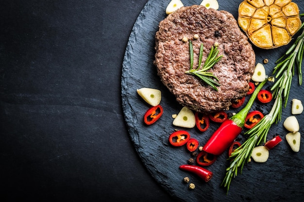 Fried fresh large beef burger with herbs and garlic on black slate top view space for text