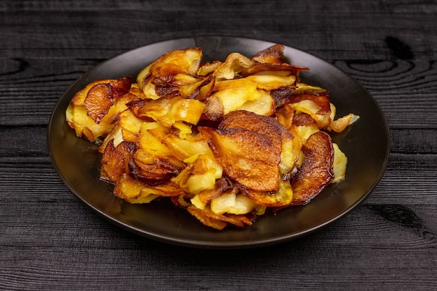 Fried homemade potato chips in a black plate on a wooden rustic background.