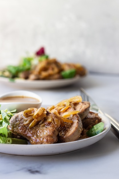 Fried juicy pork chops with caramelized onion and sauce served with green salad and beans