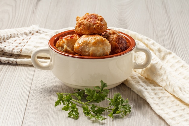 Fried meat cutlets in white ceramic soup bowl, branch of fresh parsley and kitchen towel on gray wooden table