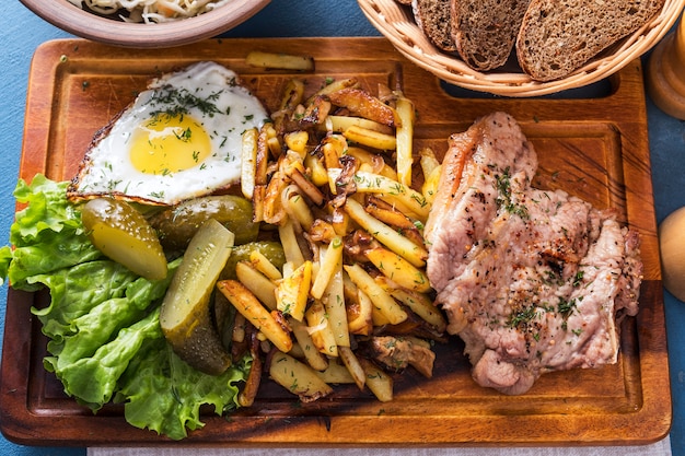 Fried meat with potatoes, pickles and a fried egg