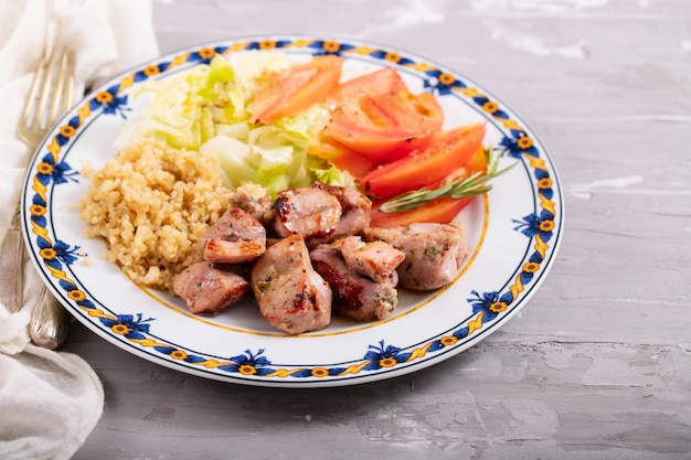 Fried meat with quinoa and fresh salad on plate on ceramic background