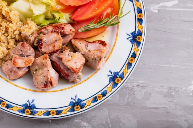 Fried meat with quinoa and fresh salad on plate on ceramic background