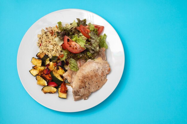 Fried meat with salad and vegetables on white plate on blue