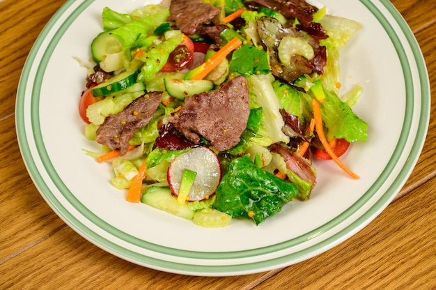 Fried meat with vegetables. Salad with meat, tomatoes, peppers, cucumbers and salad on wooden background