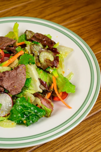 Fried meat with vegetables. Salad with meat, tomatoes, peppers, cucumbers and salad on wooden background