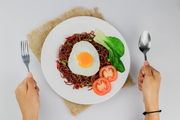 Fried noodles served with fried eggs and vegetables on a plate