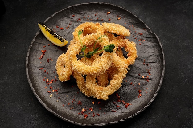 Fried onion rings in batter with spices on a black plate on a black background