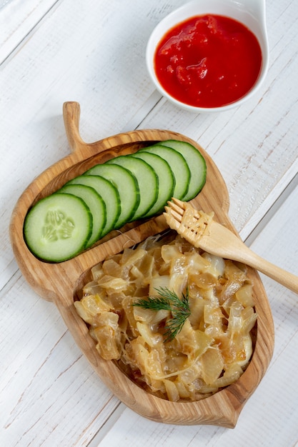 Fried onions with cheese and cucumber on a wooden plate beside tomato sauce