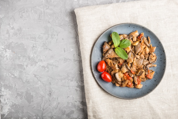 Fried oyster mushrooms with tomatoes on gray concrete background 