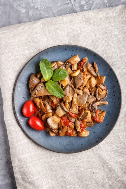 Fried oyster mushrooms with tomatoes on gray 