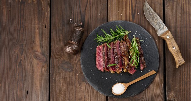 Photo fried piece of beef ribeye cut into pieces on a black board, rare degree of doneness. delicious steak, copy space