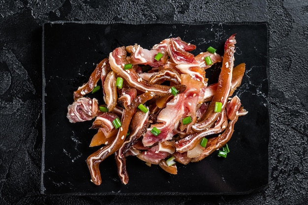 Fried pig ears with sesame seeds and green onions Fried pork ears in korean style with spicy sauce Black background Top view