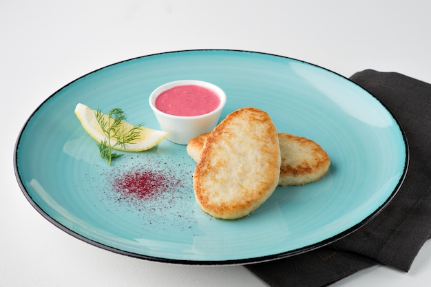 Fried pike cutlets with lemon, vendure and pink sauce on turquoise plate and black napkin on white background