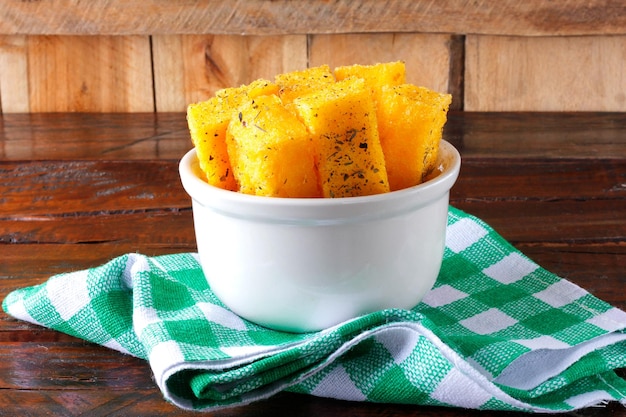 Fried polenta sticks in white ceramic bowl on rustic wooden table