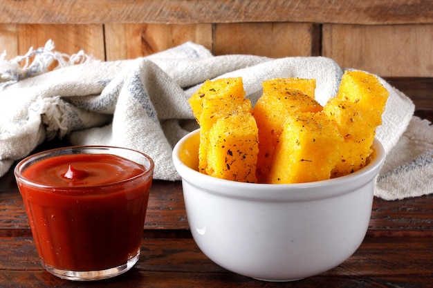 Fried polenta sticks in white ceramic bowl on rustic wooden table