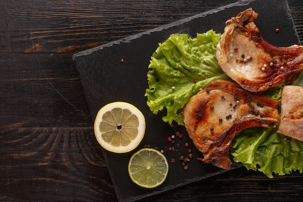 Fried pork chop on a black plate with spices, herbs and tomatoes.