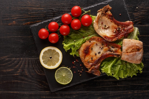 Fried pork chop on a black plate with spices, herbs and tomatoes.