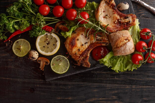 Fried pork chop on a black plate with spices, herbs and tomatoes.