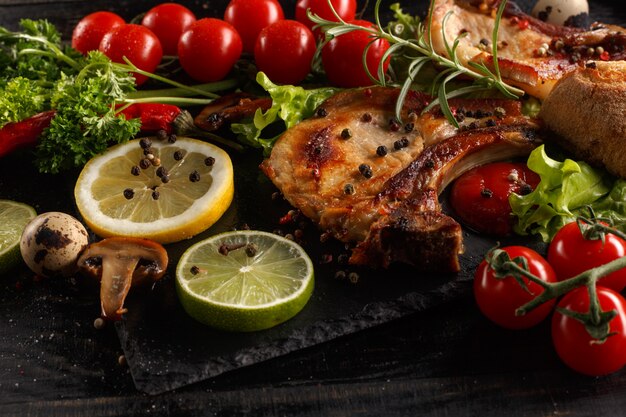 Fried pork chop on a black plate with spices, herbs and tomatoes.