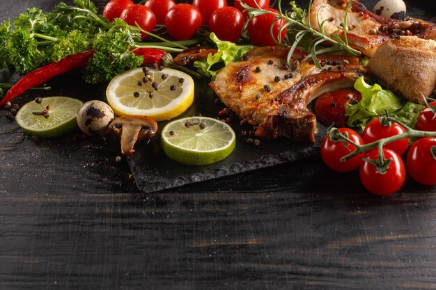 Fried pork chop on a black plate with spices, herbs and tomatoes.