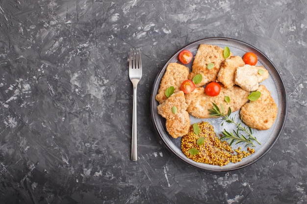 Fried pork chops with tomatoes and herbs on a gray ceramic plate on a black concrete background.  top view, copy space.