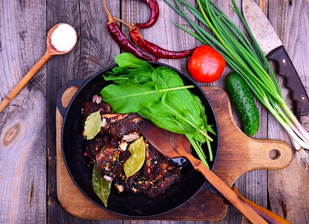 Fried pork ribs in spices on a black cast-iron frying pan