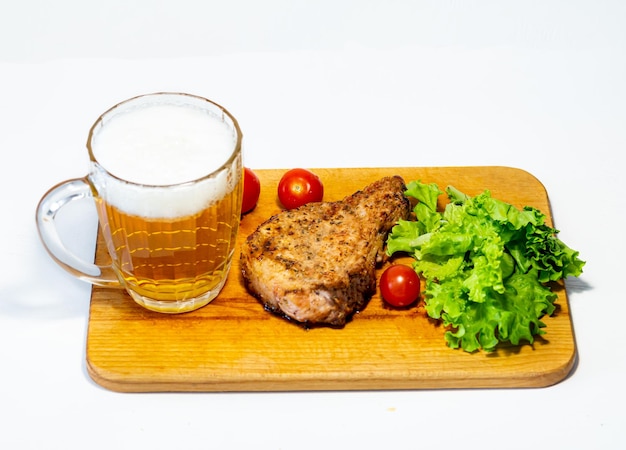 Fried pork steak with cherry tomatoes and lettuce on a wooden board on a white background