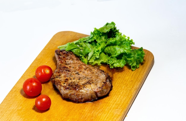 Fried pork steak with cherry tomatoes and lettuce on a wooden board on a white background