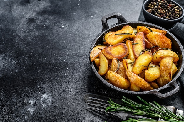 Fried potato wedges, French fries in a pan. Black background. Top view. Copy space