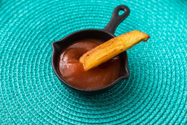 Fried potatoes dipped in ketchup on a turquoise background