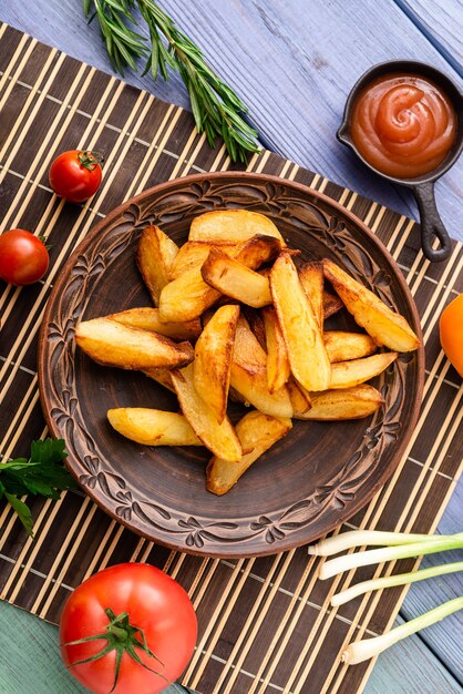 Fried potatoes in large pieces on a plate on the table with different vegetables.