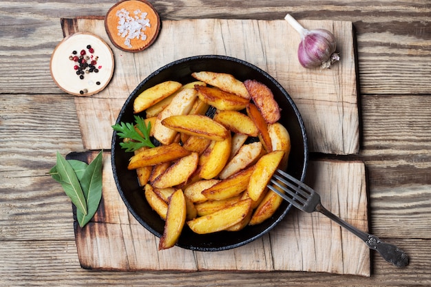 Fried potatoes wedges in a pan on wooden table. Top view.