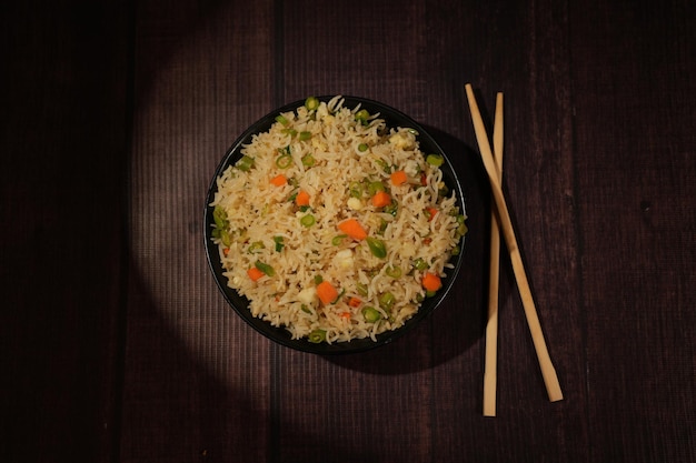 Fried rice bowl with chopsticks on a dark wooden background top angle