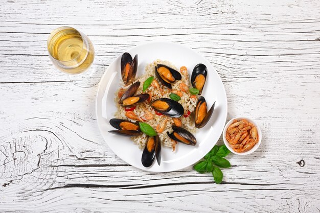 Fried rice with seafood mussels, shrimps and basil in a plate with wineglass on white cracked wooden table. Top view.