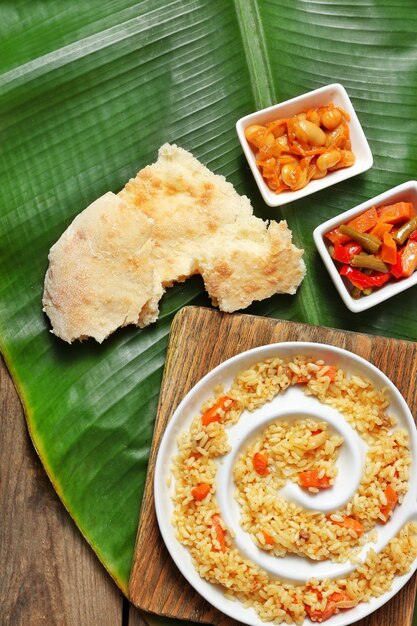 Fried rice with vegetables and flat bread on banana leaf over wooden background