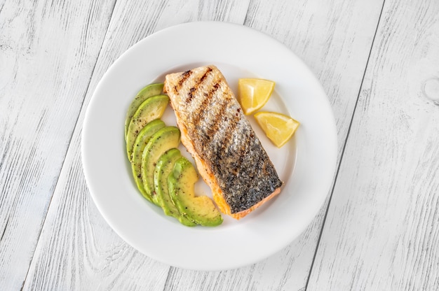 Fried salmon with avocado slices and lemon wedges