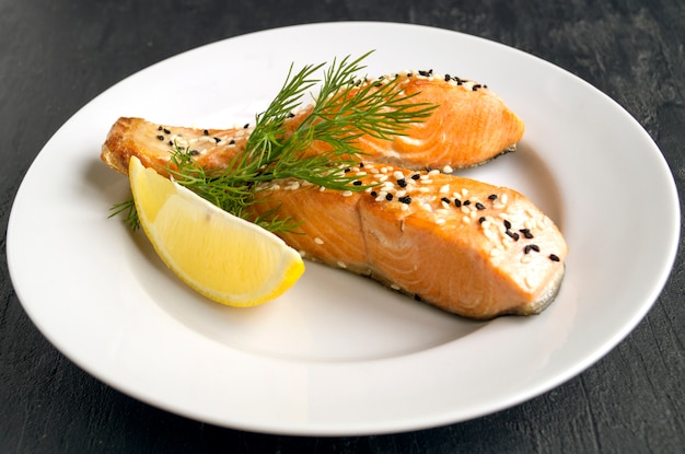 Fried salmon with sesame, lemon, dill on a white plate. Selective focus.