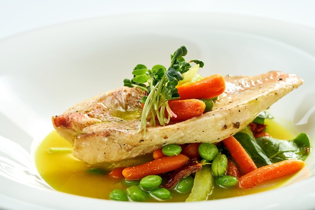 Fried Sea bass fillet with stewed vegetables and orange sauce in a white plate. Isolated on grey surface.