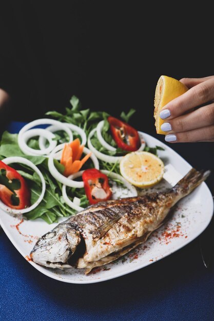 Fried sea bream cupra fish on white plate with onion garden rocket and lemon slices