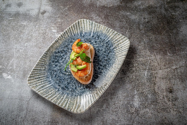 Fried shrimp and avocado sandwich on a plate of greens against a gray stone table