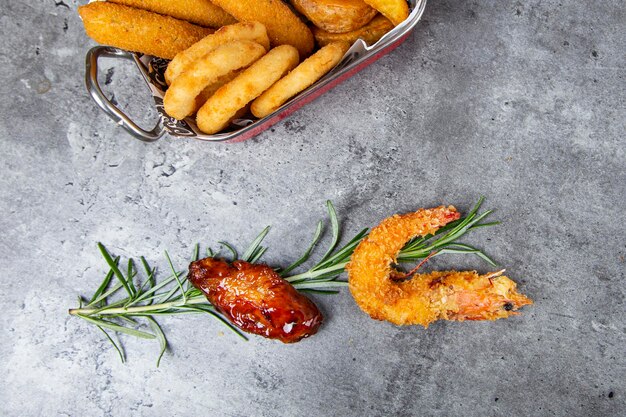 Fried shrimp and chicken wing top view with fried potatoes and rosemary in grey background