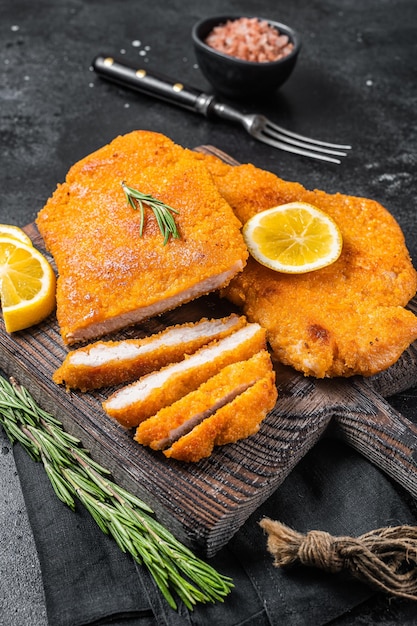 Fried sliced weiner schnitzel on a wooden board with herbs Black background Top view