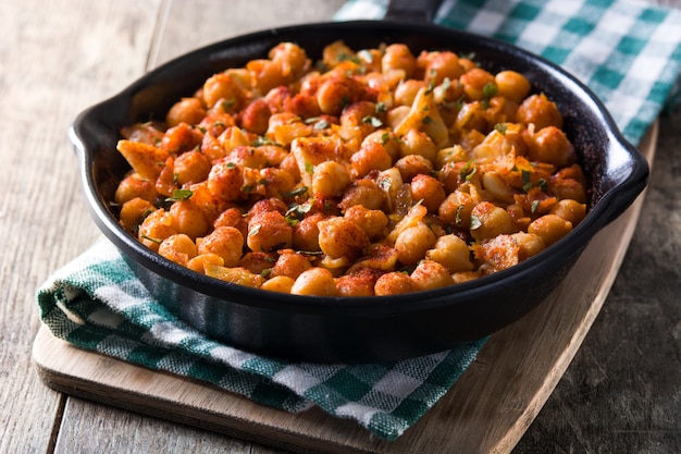 Fried spicy chickpeas in frying pan on wooden table