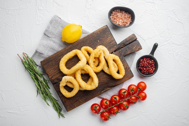 Fried squid rings breaded calamari appetizer set, on serving board, on white stone table background, top view flat lay