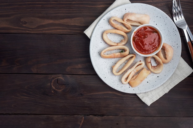 Fried squid rings with tomato sauce and lemon. Dark wooden background copy space. Top view.