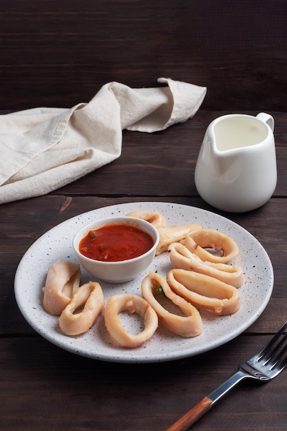 Fried squid rings with tomato sauce and lemon. Dark wooden background copy space.