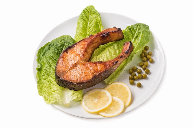 Fried trout with a piece of lettuce, lemon and green peas on a white background