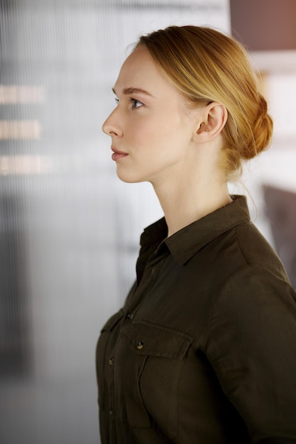 Friendly adult casual dressed business woman standing straight in sunny office. Business headshot