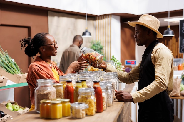 Friendly African American male vendor advising and assisting a black woman with fresh pasta suggestions The store offers organic produce bulk items and plasticfree packaging